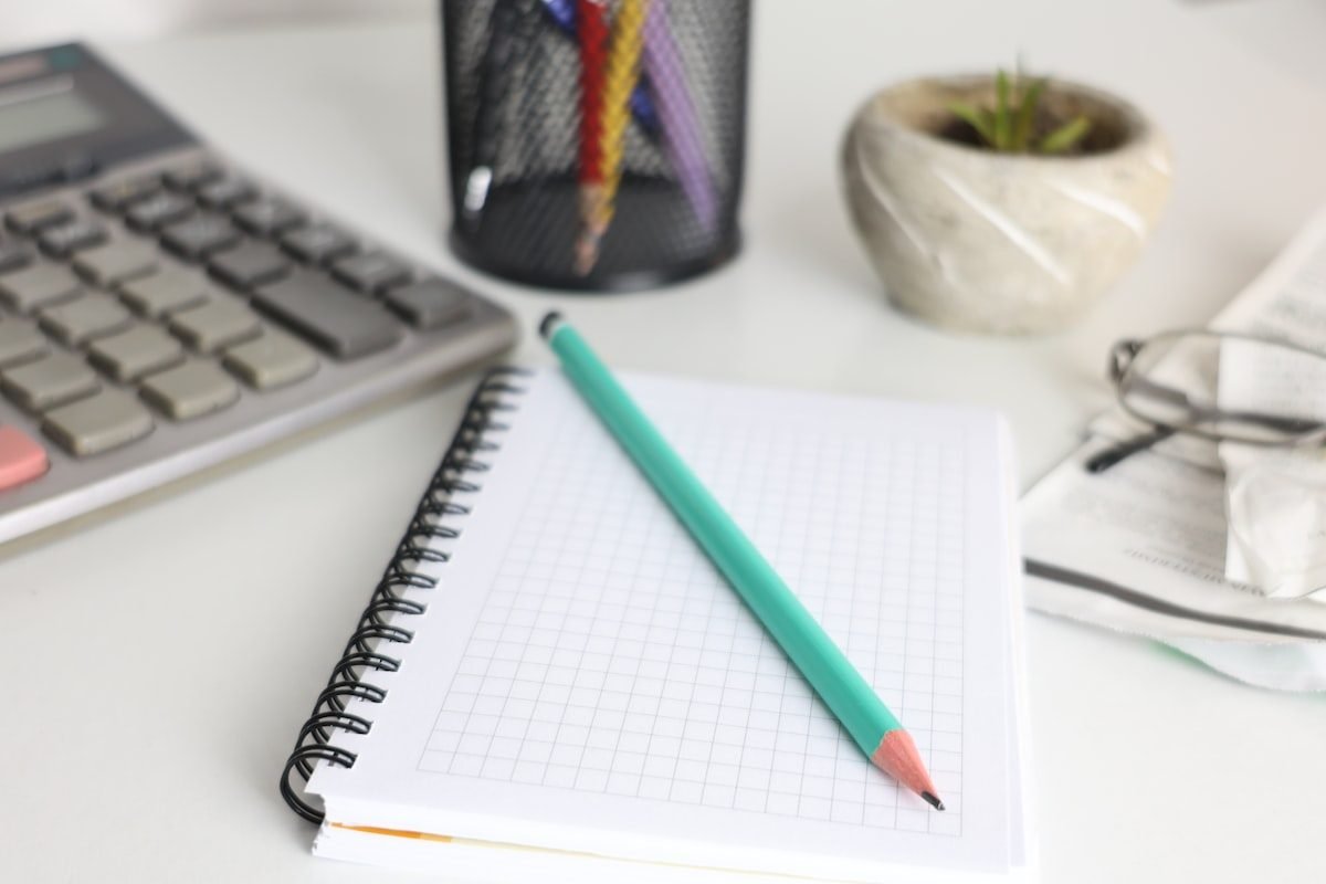 Cuaderno cuadriculado y lápiz junto a una calculadora sobre un escritorio blanco